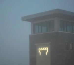 The illuminated Watchtower sign shines through the haze at Warwick